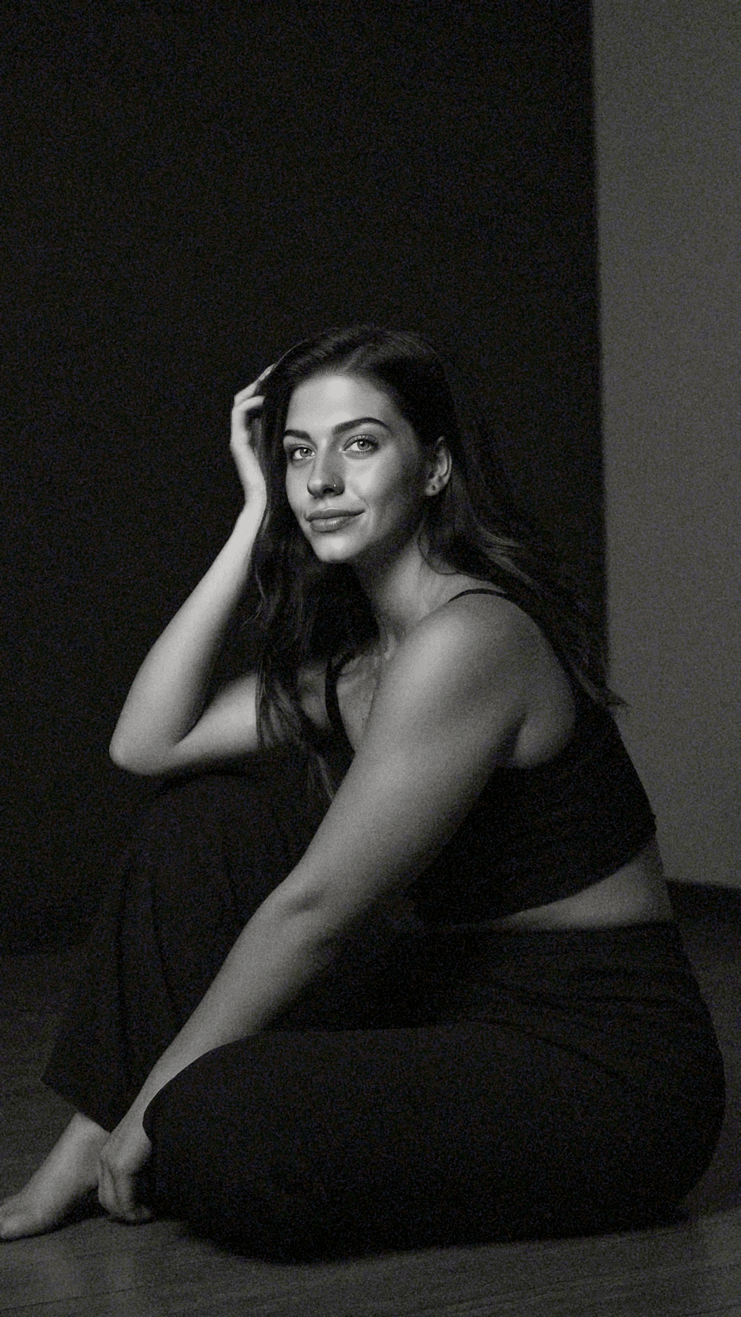 Grainy black and white studio portrait of a woman sitting on the floor.